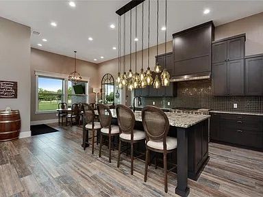 Modern kitchen with dark cabinets, island, and wooden floor; dining area visible.