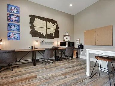 Home office with desks, artwork, map, chairs, and a whiteboard on a wood floor.