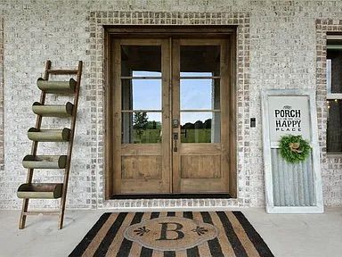 Wooden double doors with glass panels, brick wall, welcome mat, ladder planter, and