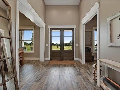 Entryway with double doors, wood floors, neutral walls, windows, and a console table.