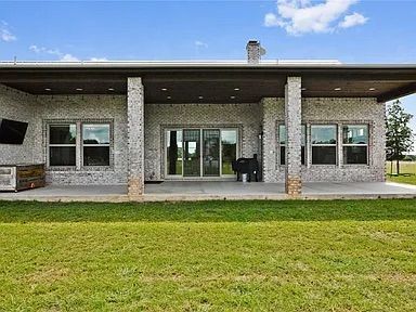 Back of a brick house with a covered patio, featuring a grassy lawn and sliding glass doors.
