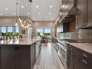 Modern kitchen with island, dark cabinets, stainless steel appliances, and light wood floors.
