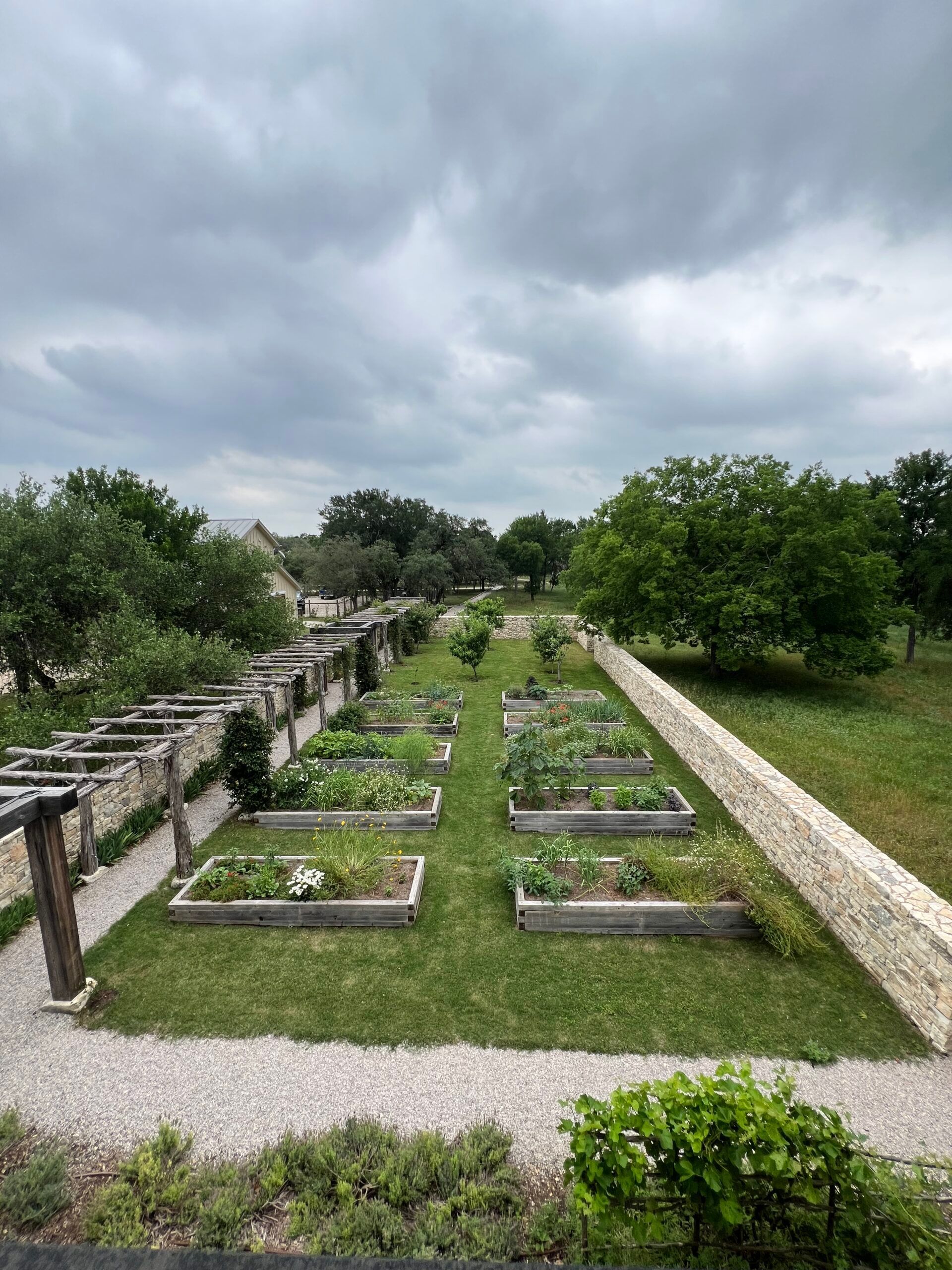Raised garden beds, stone pathways, and trellises under an overcast sky.