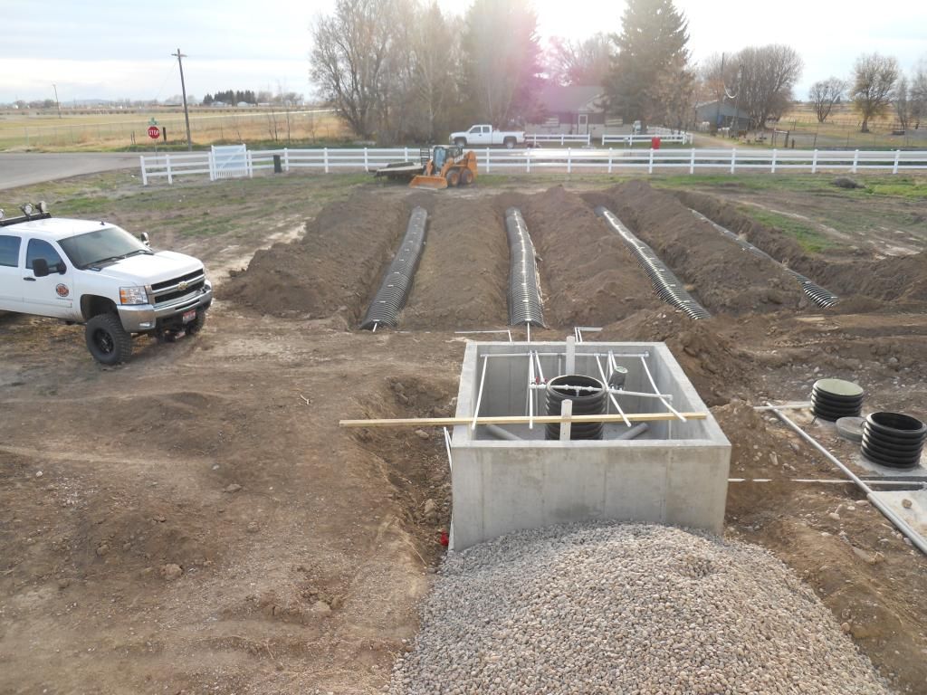Construction site with a concrete septic tank and trenches, dirt, gravel, and a truck.