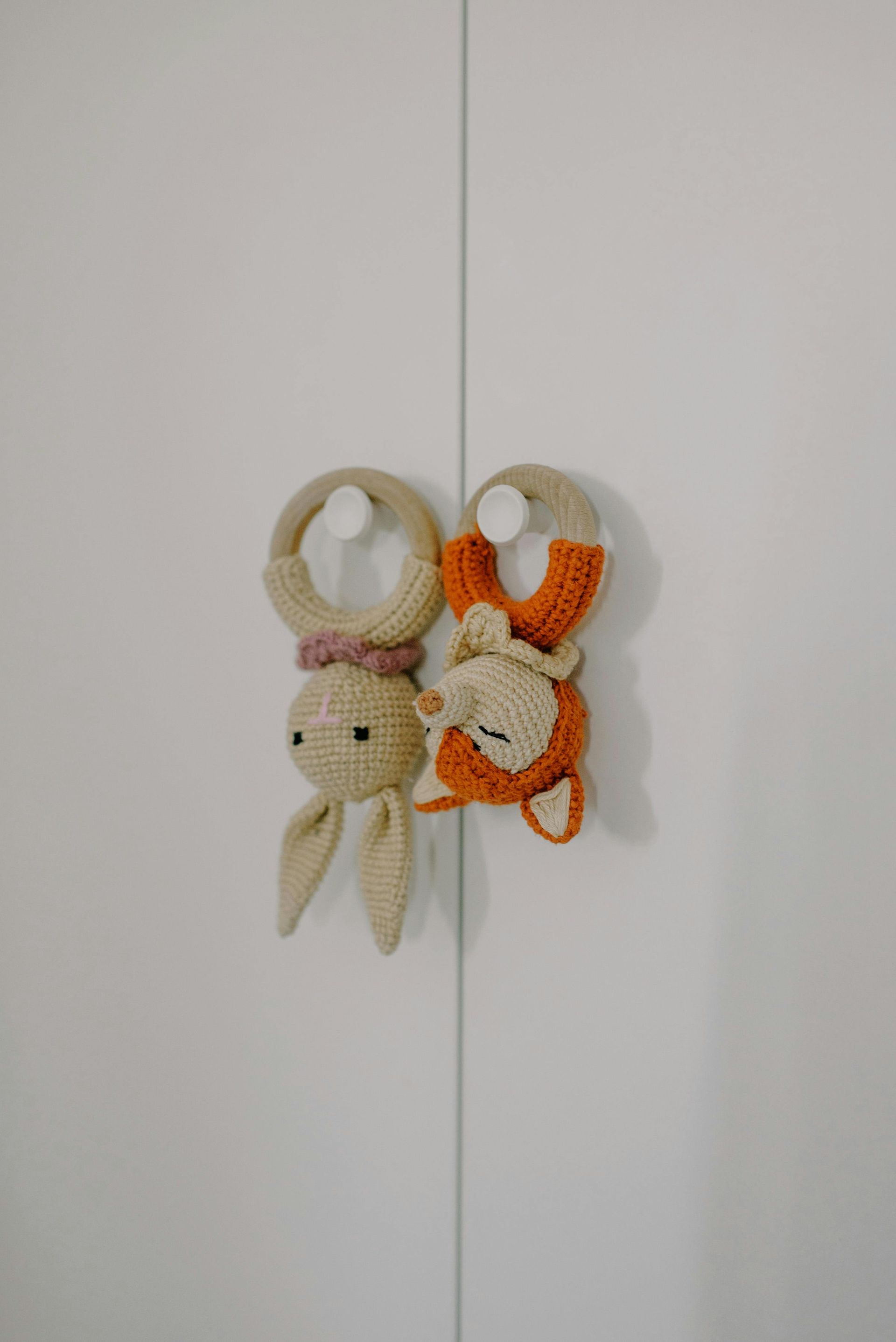 Twee gehaakte babyspeeltjes hangen aan witte kastdeuren. Het ene is een konijntje, het andere een vosje.
