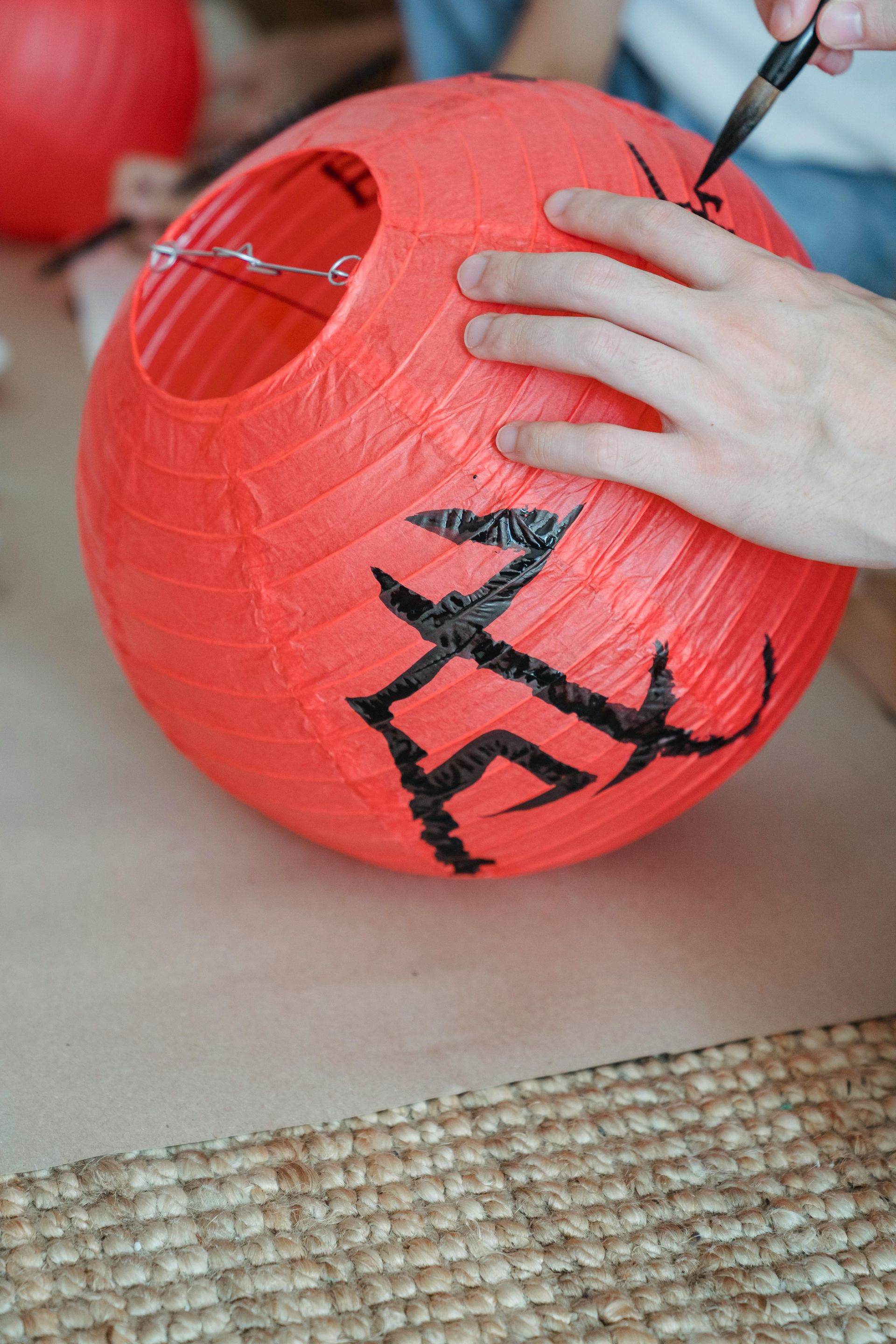 Iemand schrijft met een zwarte stift zwarte letters op een rode papieren lantaarn.