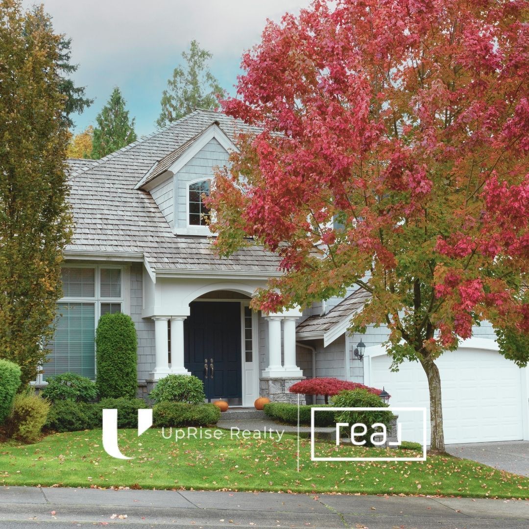 A suburban two-story home with a white garage door and vibrant autumn trees in the yard, with UpRise Realty branding.