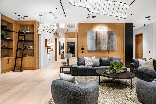 Modern living room with wood built-in shelving rolling ladder gray sofas round coffee table and large abstract wall art.