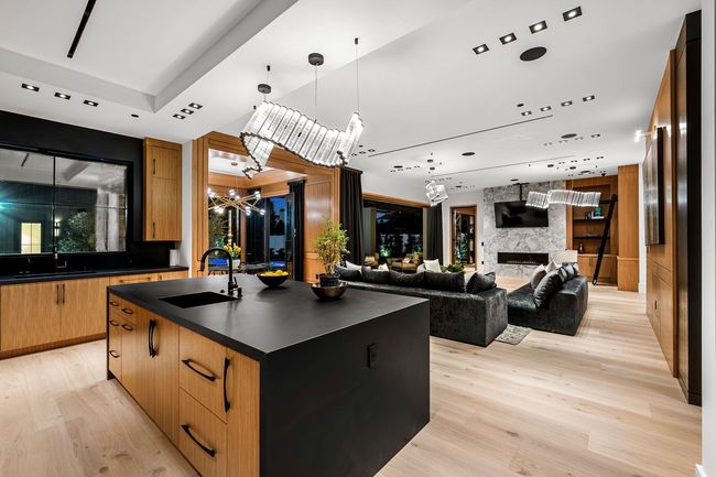 Open-plan kitchen and living area with black island wood cabinetry statement pendant lights and marble fireplace.