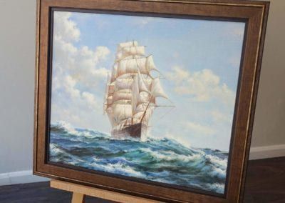 A painting of a sailboat in the ocean is on an easel.