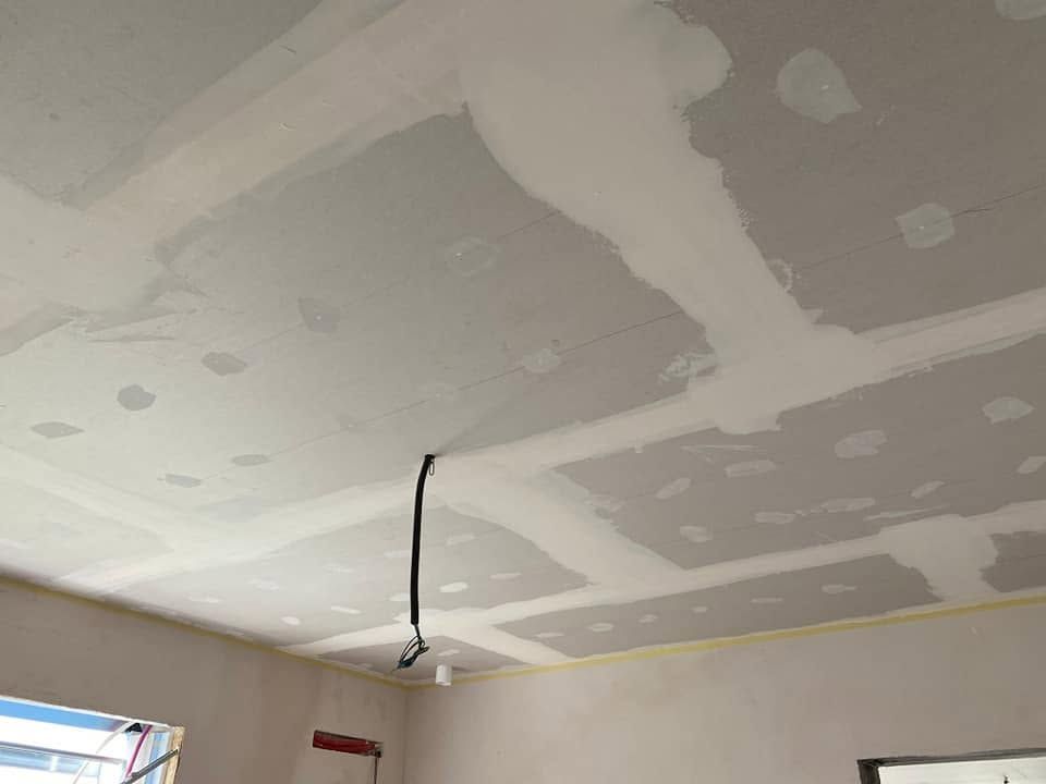 Soffitto non rifinito con giunture in cartongesso e un filo nero penzolante in una stanza in fase di ristrutturazione.