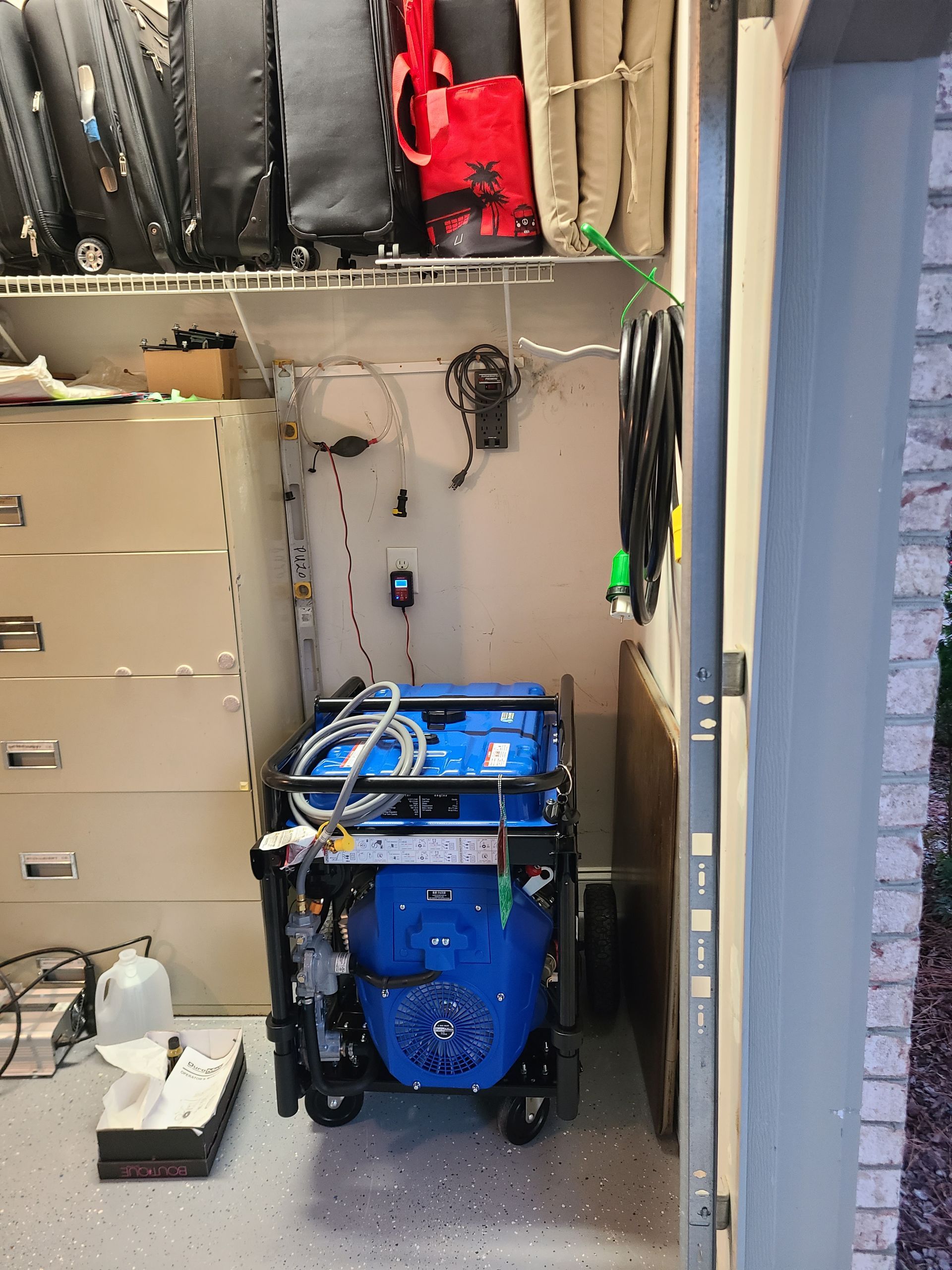 A blue generator is sitting in a closet next to a door.