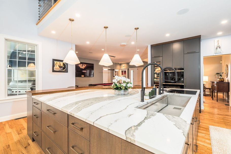 Modern kitchen with large island, marble countertops, pendant lights, and hardwood floors
