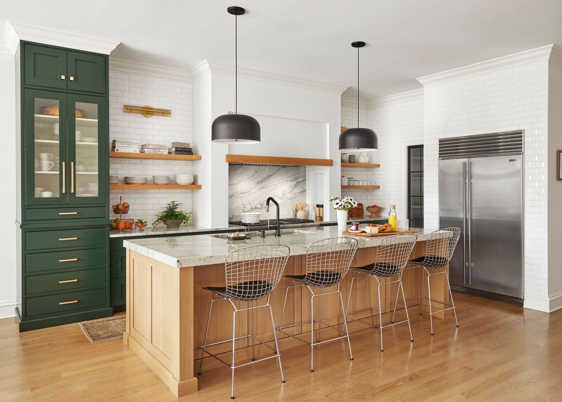Modern kitchen with green cabinets, marble island, pendant lights, and stainless steel refrigerator