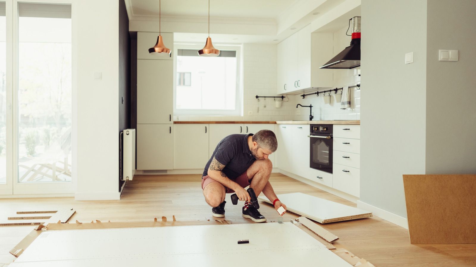 Person kneeling on a kitchen floor, installing or repairing wooden flooring in a bright, modern home