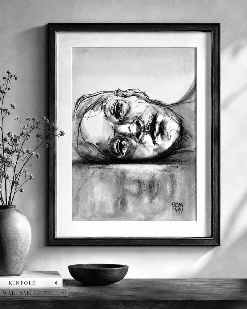 Ingelijst zwart-witportret van een liggend gezicht aan de muur boven een plank en een vaas.