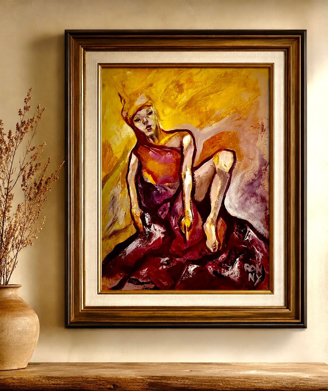 Framed abstract painting in warm reds and golds, displayed on a beige wall beside a vase of branches.