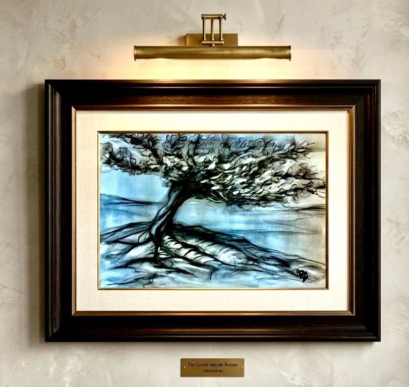 Framed watercolor of a windswept tree by water, lit by a brass picture light on a wall