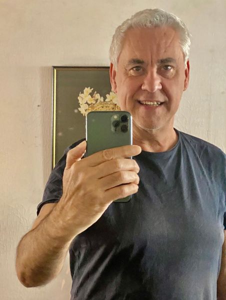 Een man in een donkerblauw T-shirt maakt een selfie in de spiegel, houdt een groene telefoon vast en staat binnen.