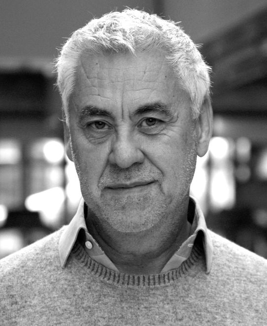 Zwart-witportret van een man in een trui, die met een neutrale uitdrukking in de camera kijkt.
