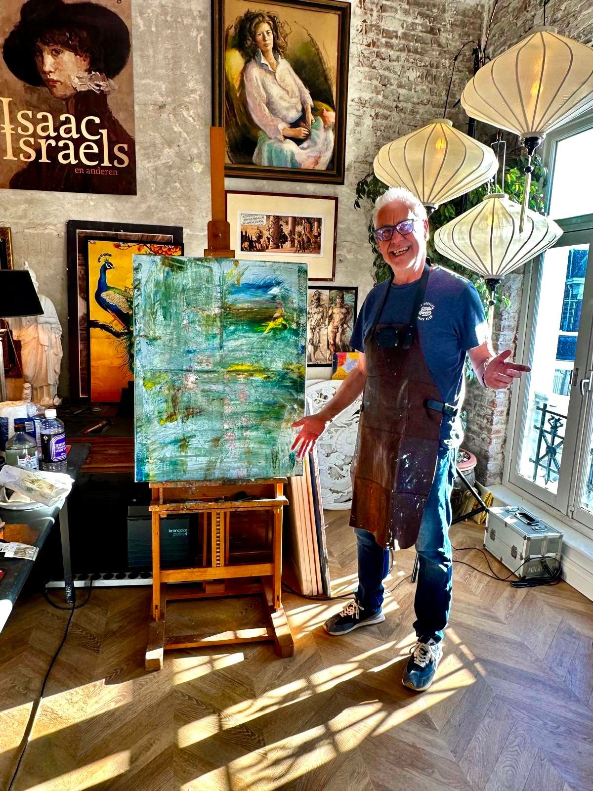 Een persoon staat naast een abstract schilderij in een kunststudio met fel zonlicht en kunst aan de muur.