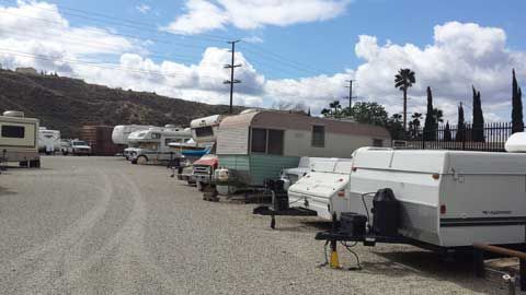 A row of trailers are parked in a gravel lot.