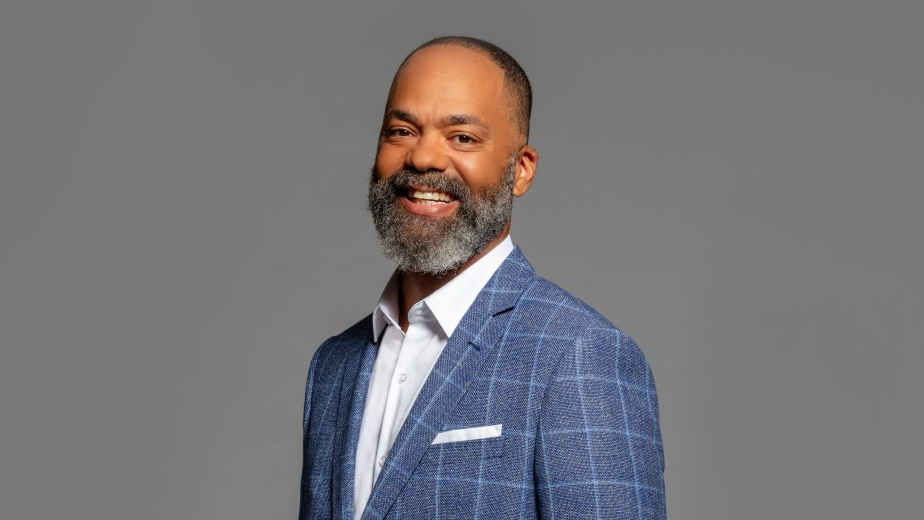 A man with a beard is wearing a blue suit and smiling.