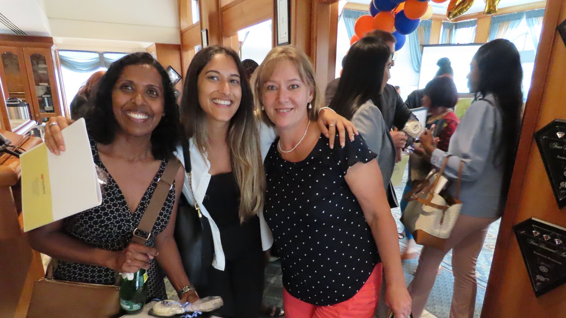 Three women are posing for a picture in a room with balloons in the background.