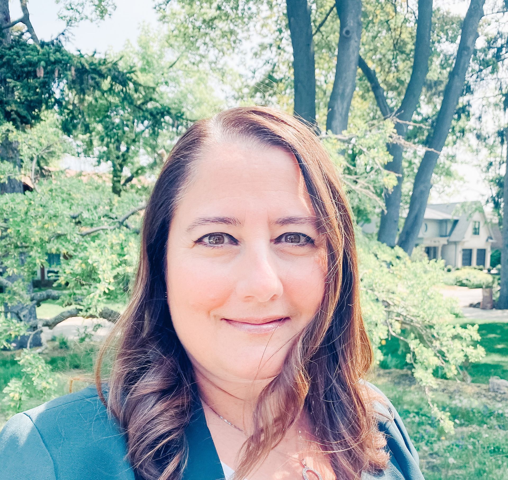 A woman is smiling for the camera in front of trees.