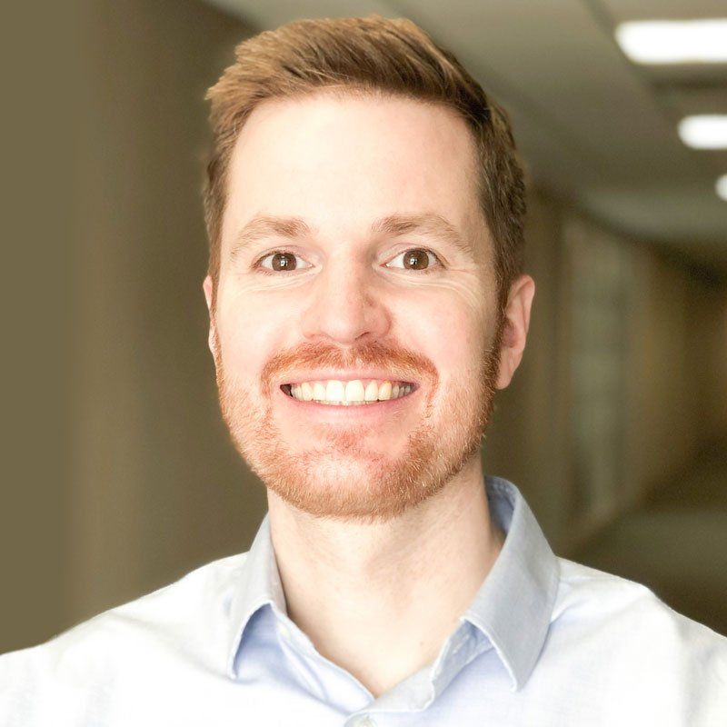 A man with a beard is smiling for the camera in a hallway.