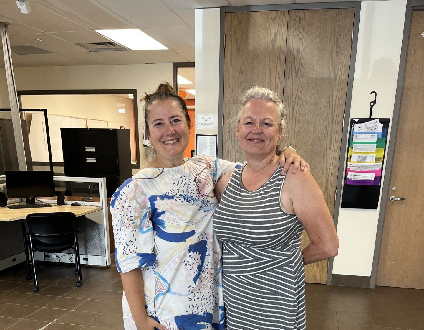 Two women are posing for a picture in an office.
