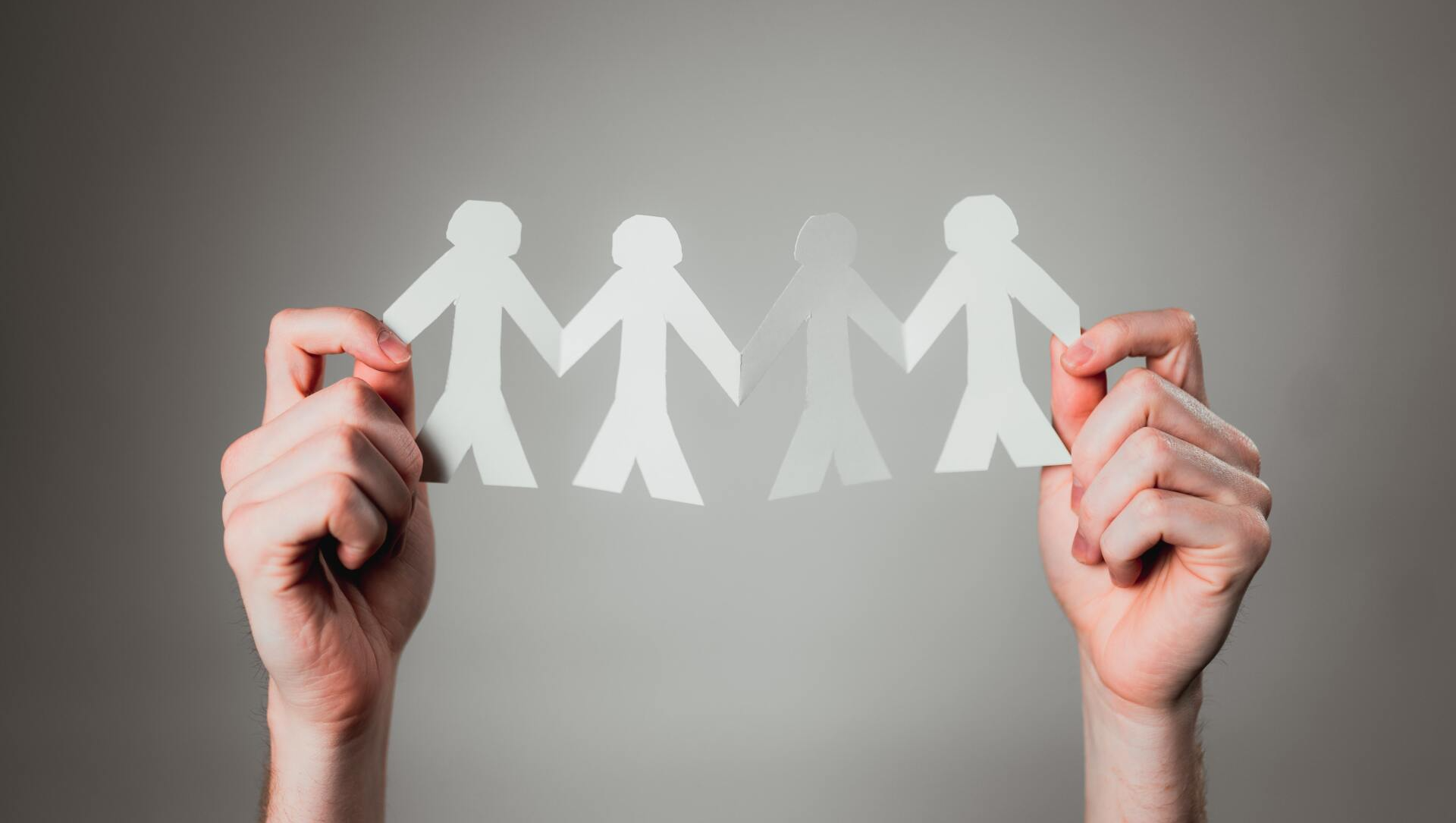 A person is holding a string of paper people in their hands.