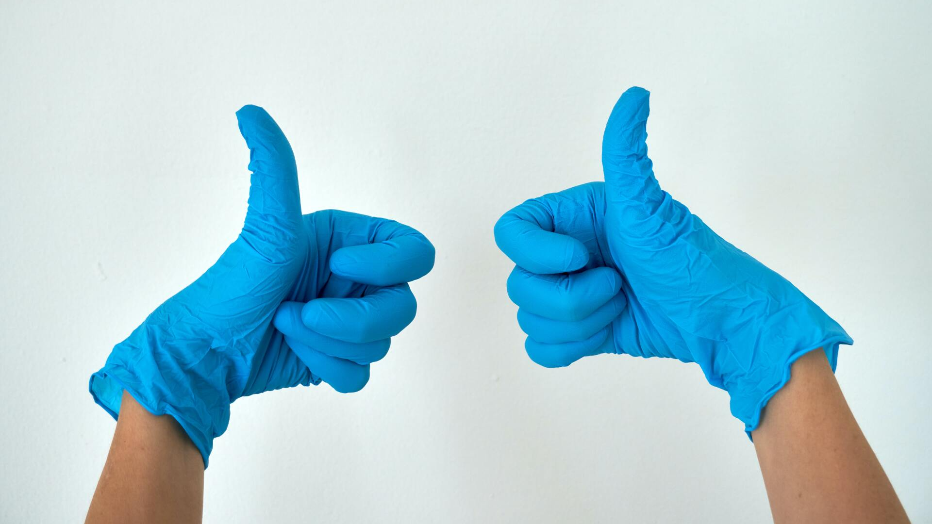 Two hands wearing blue gloves are giving a thumbs up.
