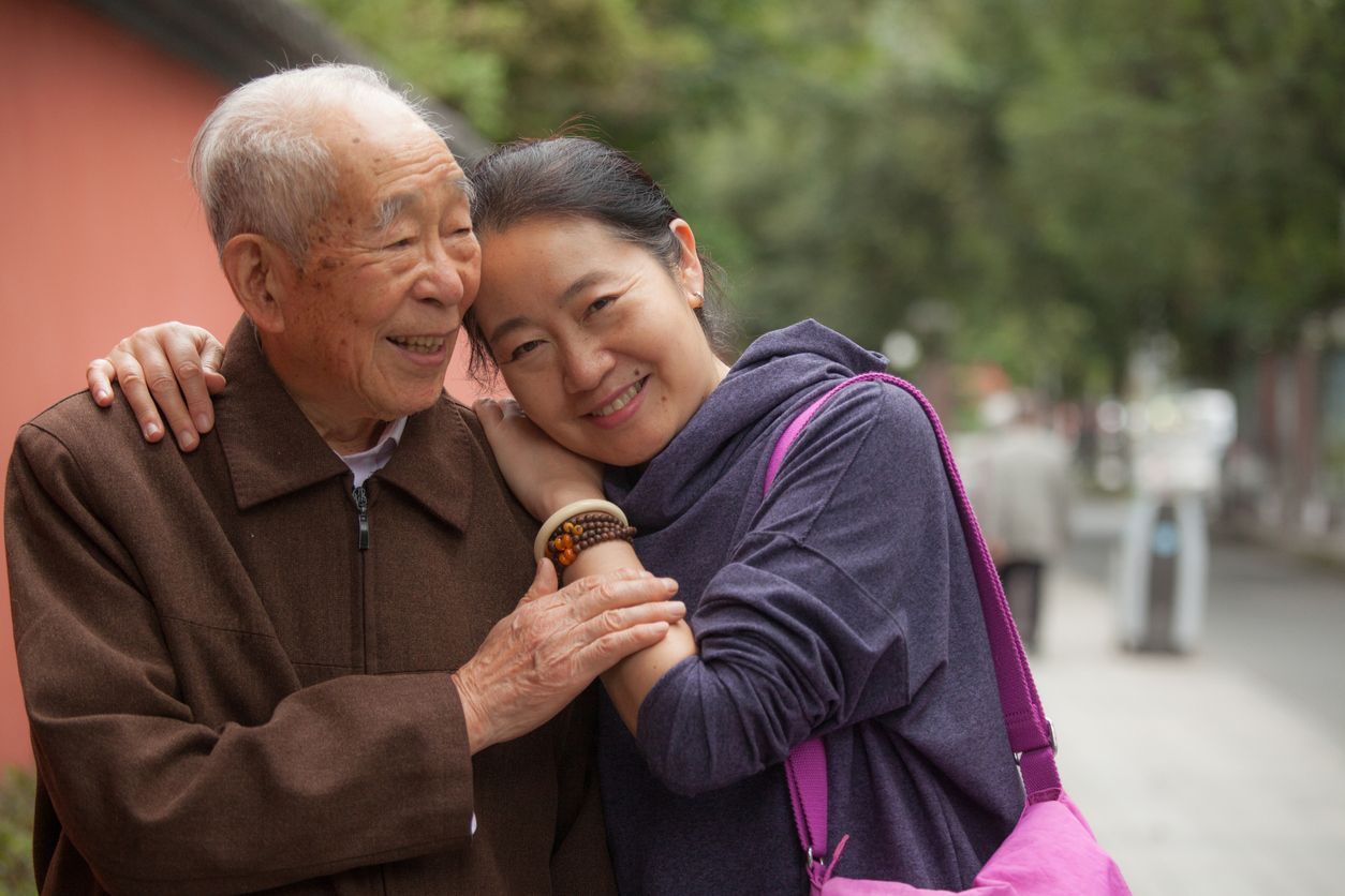 An elderly man and a young woman are hugging each other.
