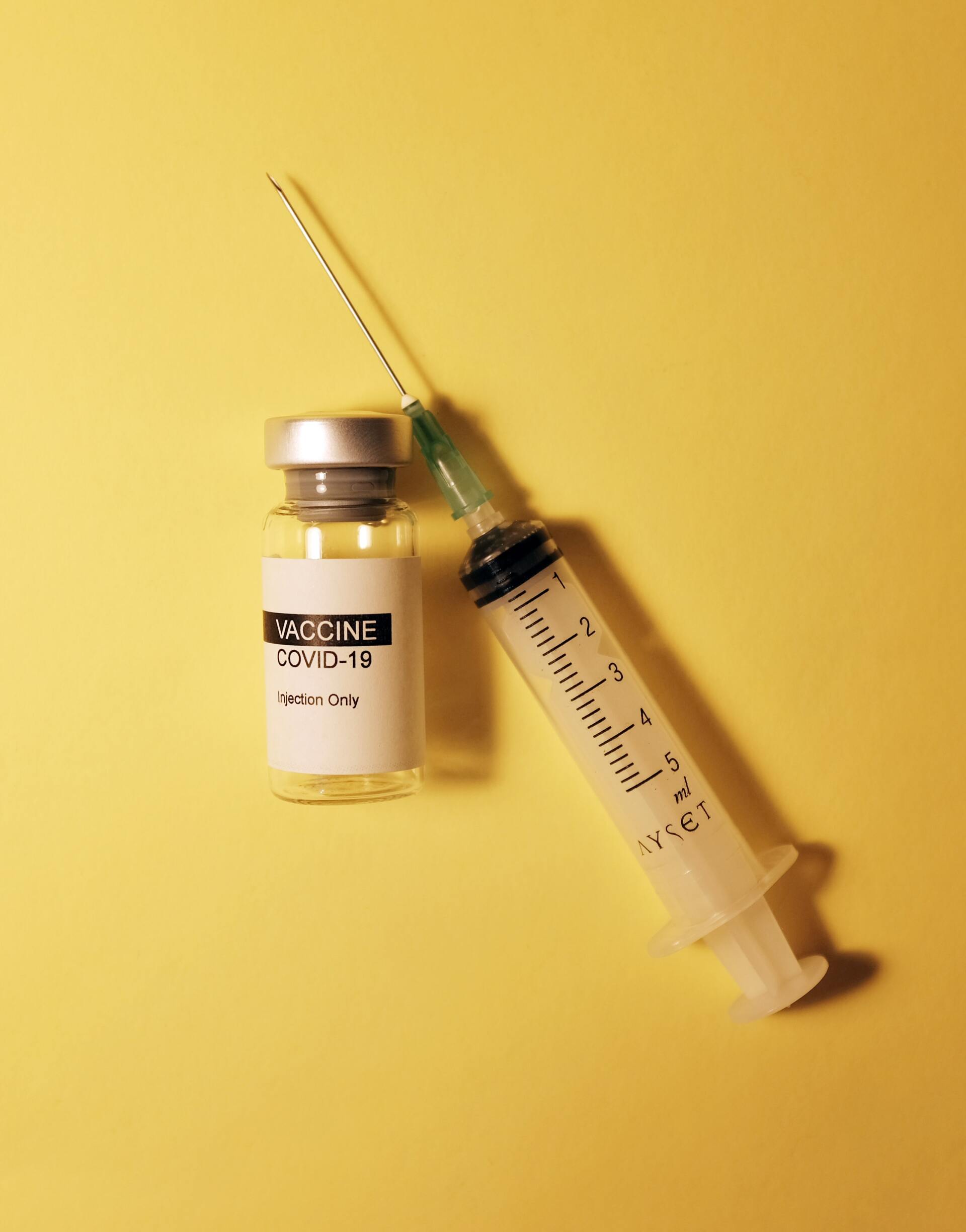 A bottle of vaccine next to a syringe on a yellow background