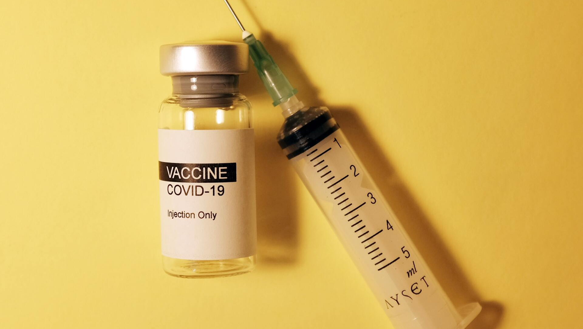 A bottle of vaccine and a syringe on a yellow background.