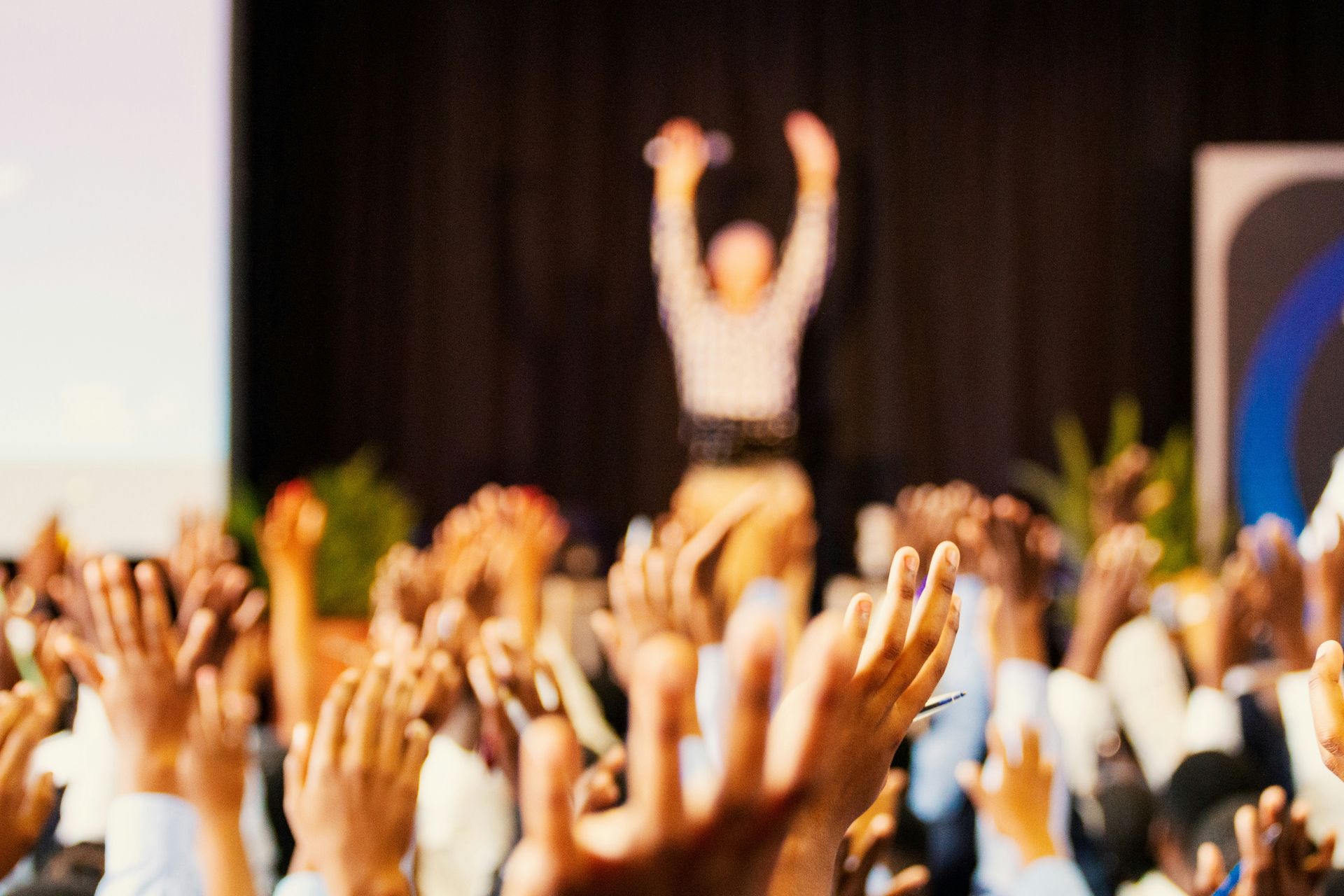 A crowd of people are raising their hands in the air at a conference.