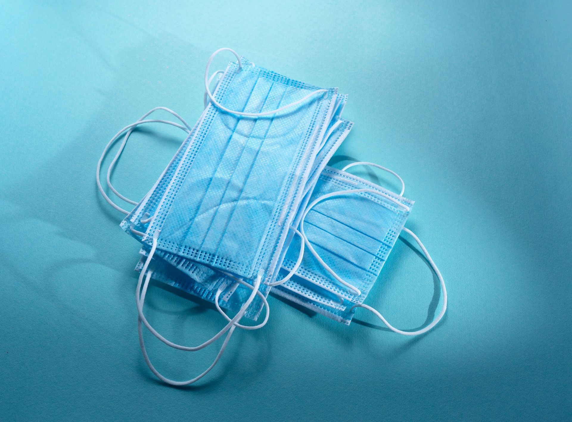 Two surgical masks are stacked on top of each other on a blue surface.