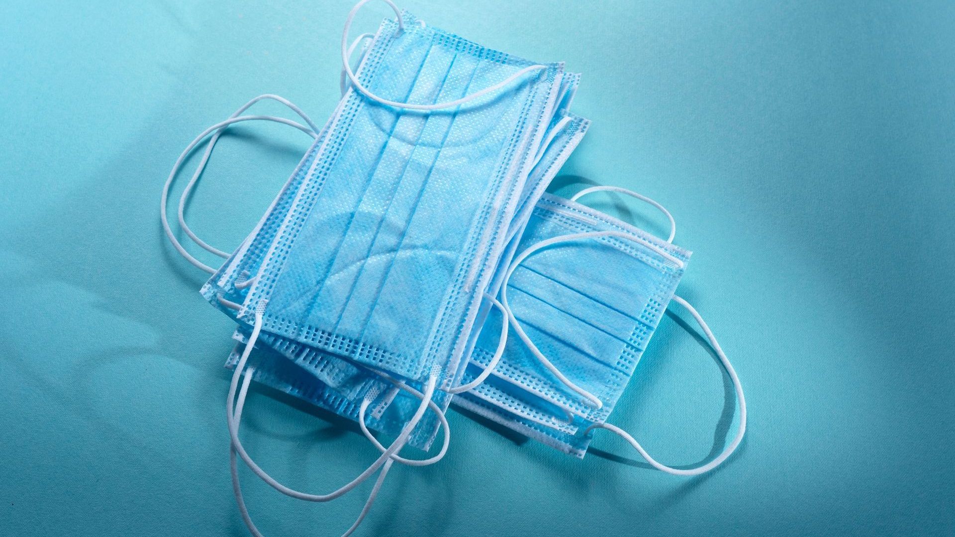 Two surgical masks are stacked on top of each other on a blue surface.