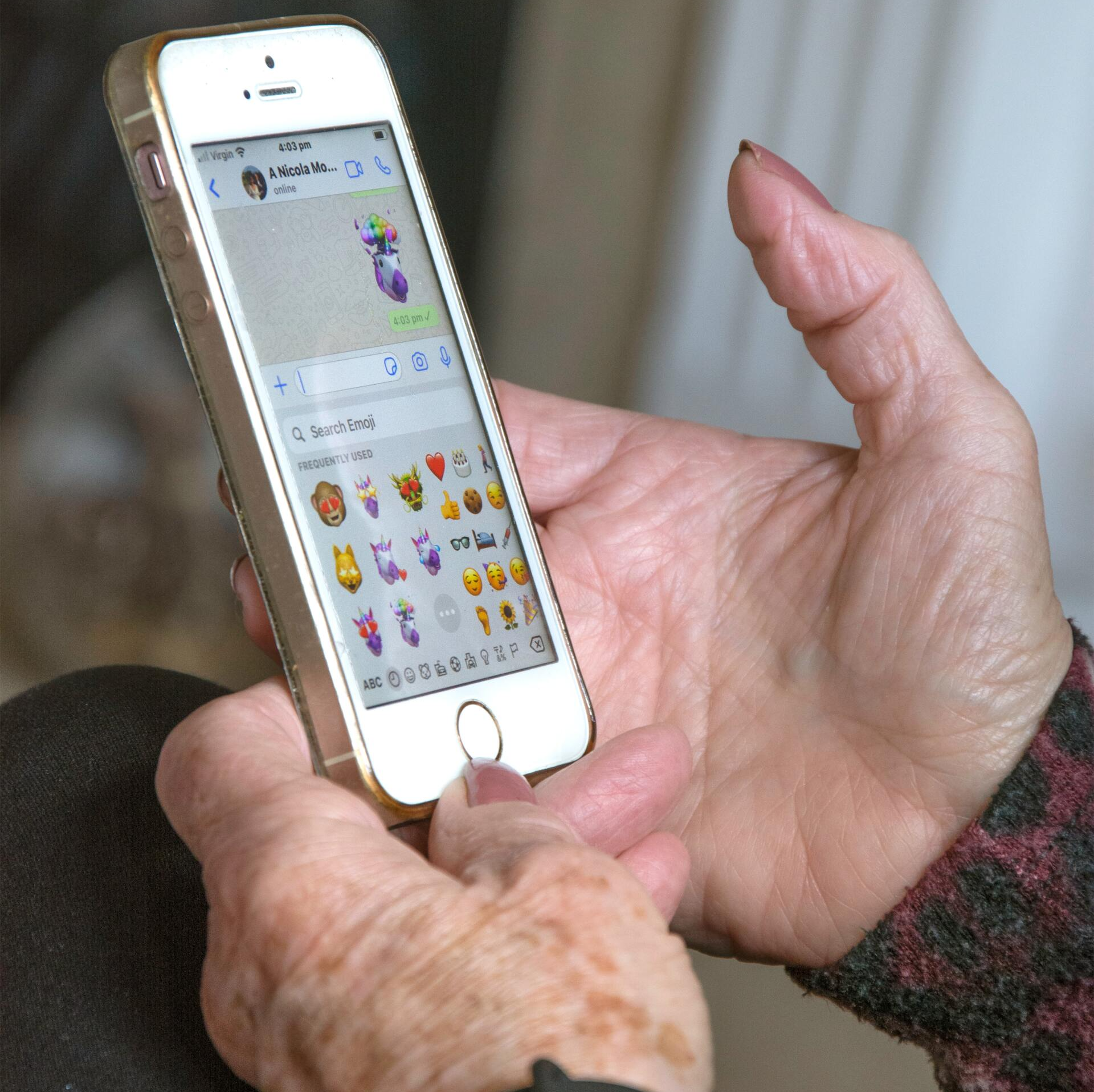 A person is holding a cell phone with emojis on the screen