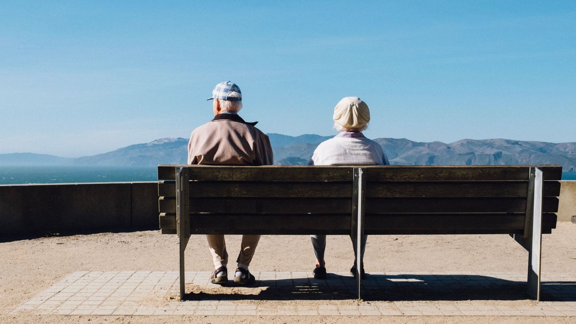 A man and a woman are sitting on a bench overlooking the ocean.