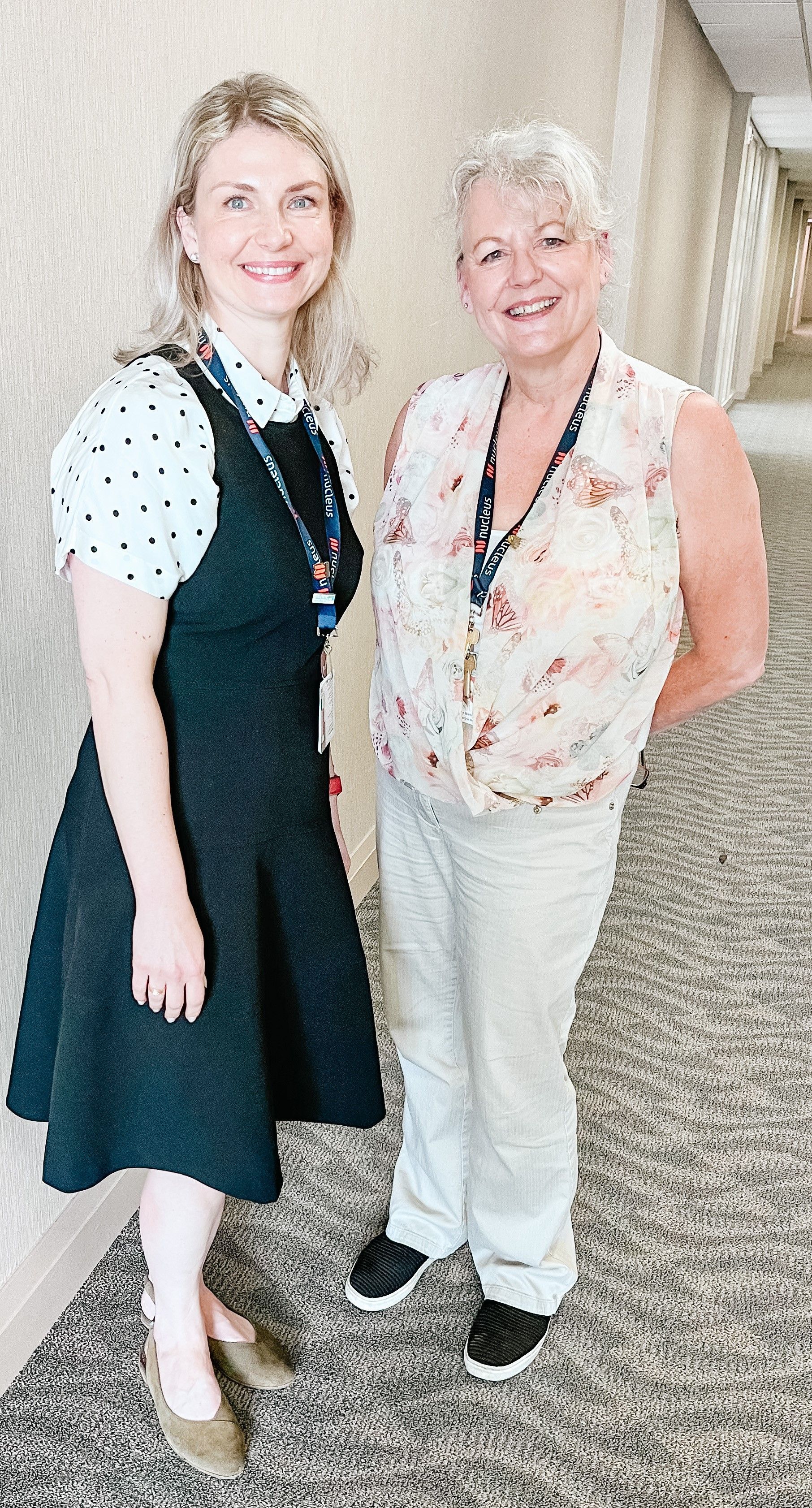 Two women are standing next to each other in a hallway.