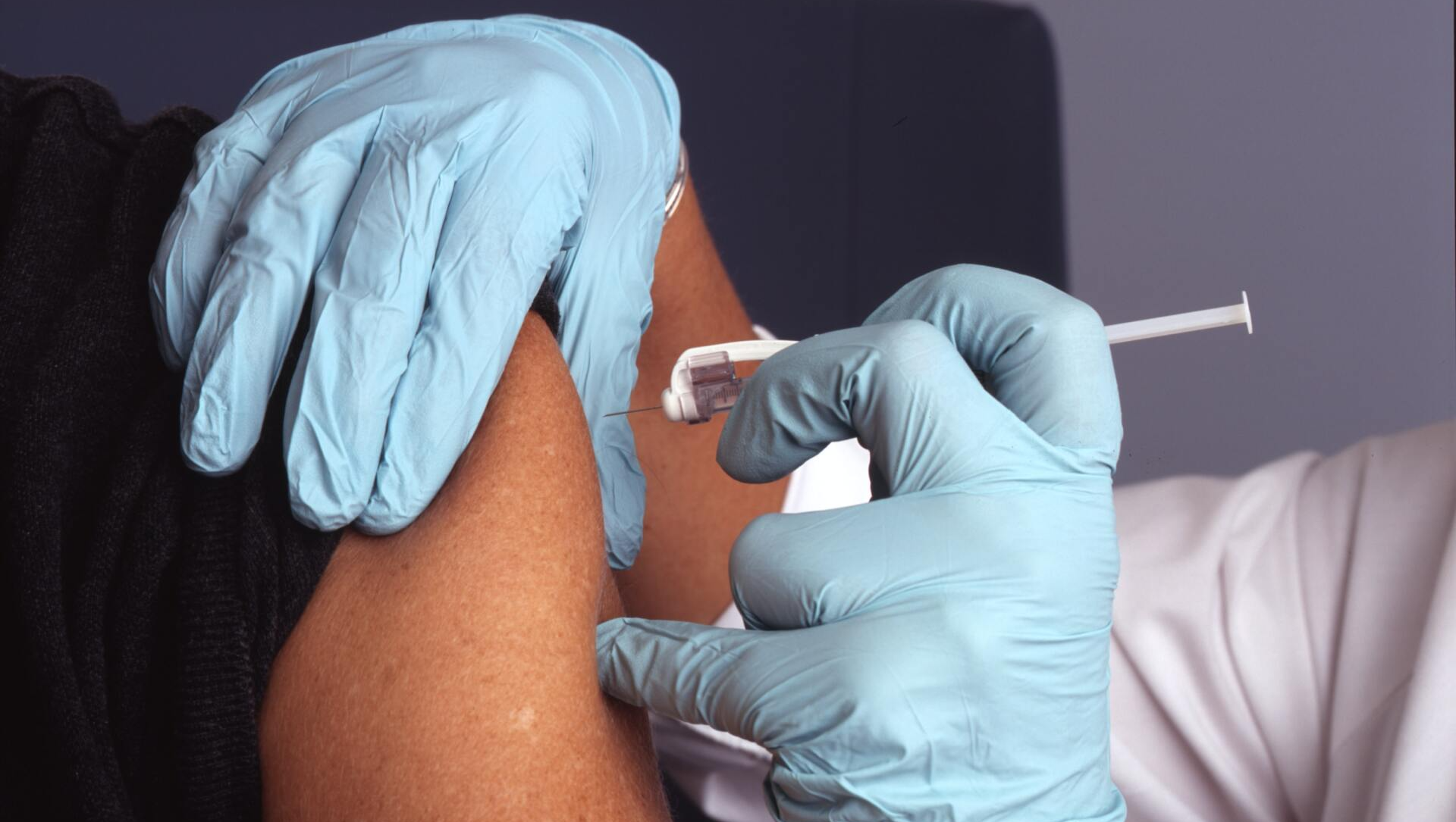 A person wearing blue gloves is getting a vaccine in their arm.