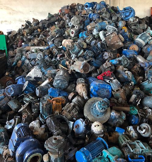 Grande cumulo di bottiglie e contenitori di plastica blu e neri ammassati in un'area di riciclaggio o smaltimento rifiuti.