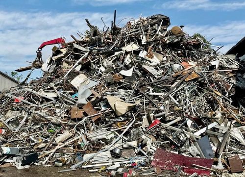 Un grande cumulo di rottami metallici e detriti in una discarica sotto un cielo azzurro.