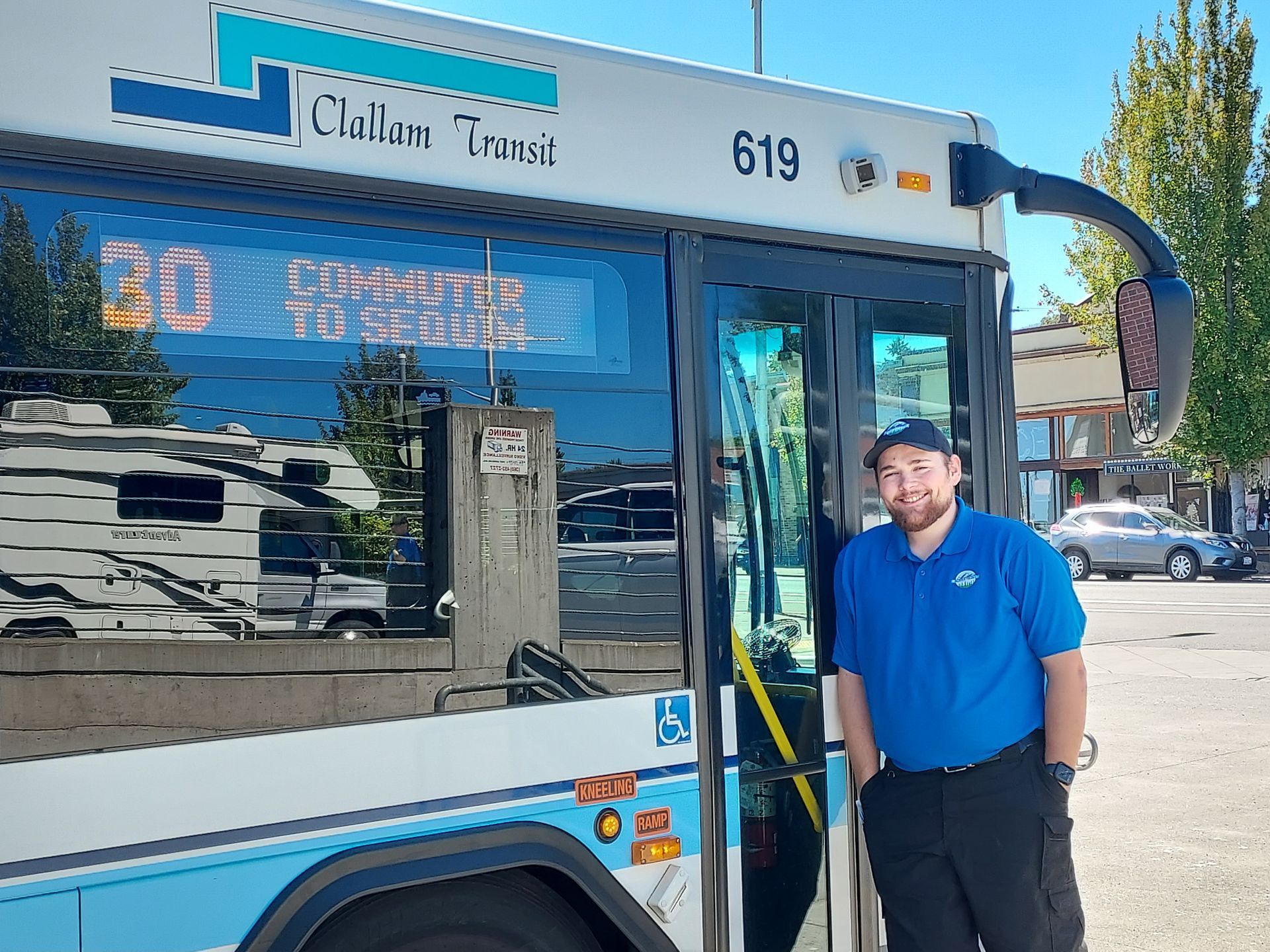 Transit operator smiling and standing in front of a bus.