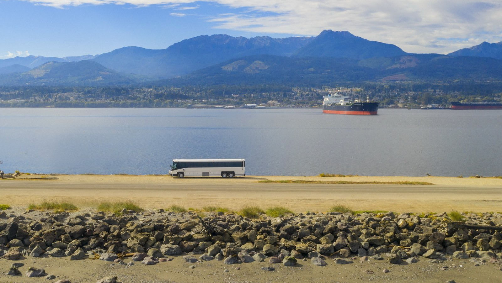 Bus parked in front of Port Angeles Harbor with the Olympic Mountains in the background.