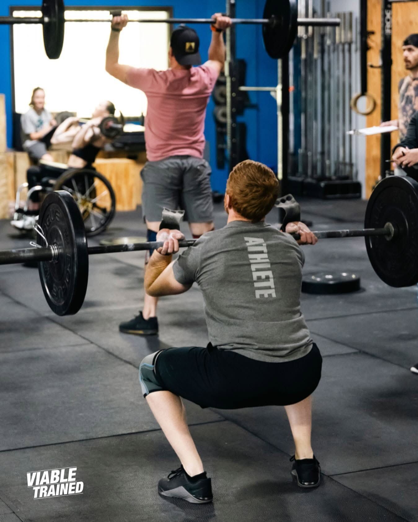 People lifting barbells in a CrossFit gym, with one person squatting in the foreground.