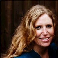 Smiling person with long wavy blonde hair against a dark brown background