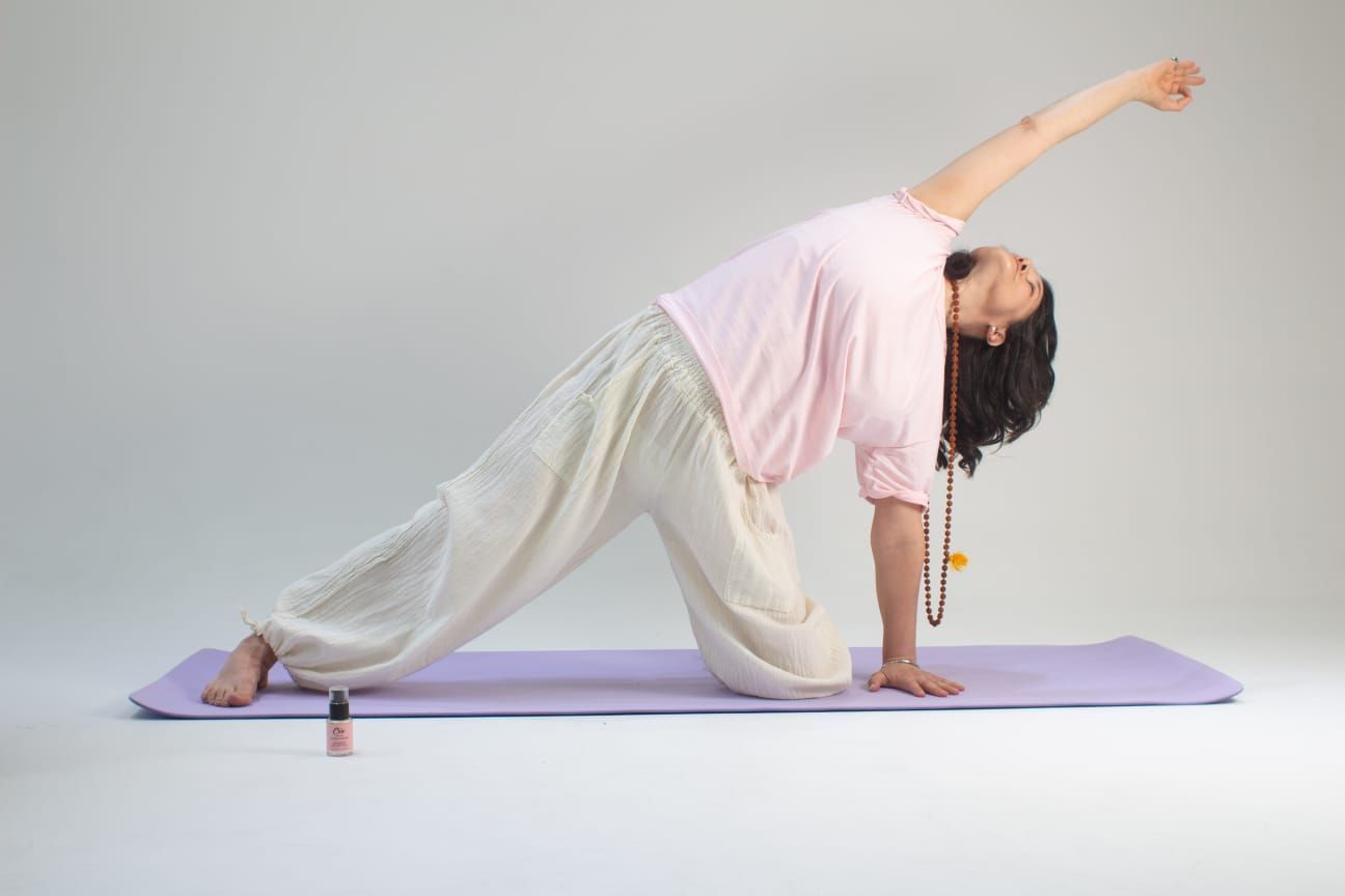 Mujer en pose de yoga, con el brazo levantado, sobre una esterilla morada, sobre un fondo blanco.